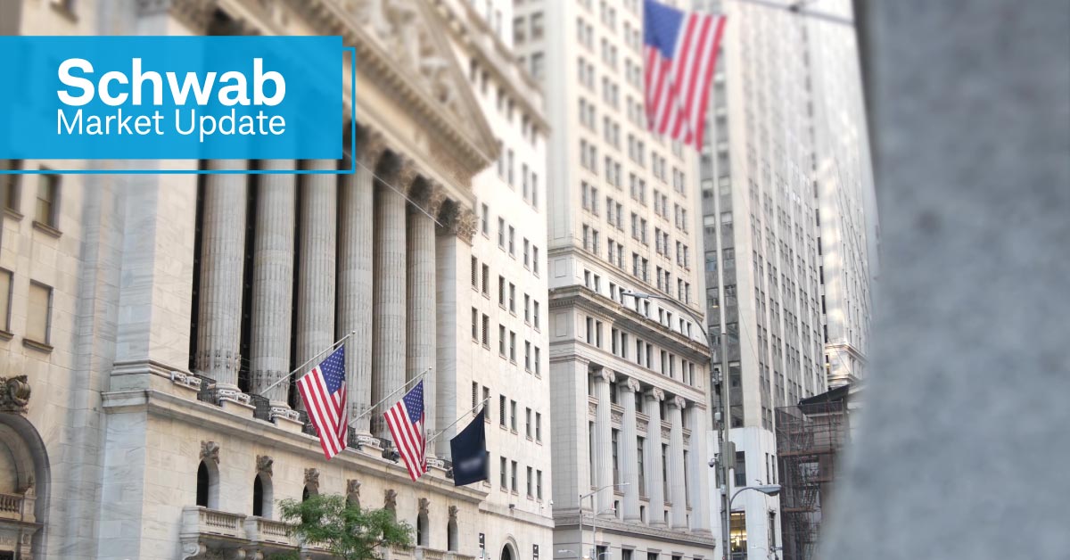 Schwab Market Update:  A view of Wall Street, including street signs, flags, and buildings.