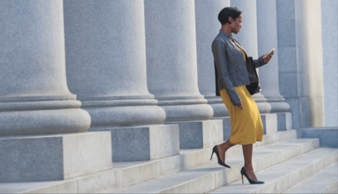 Woman in yellow skirt holding a purse and phone walks down cement stairs